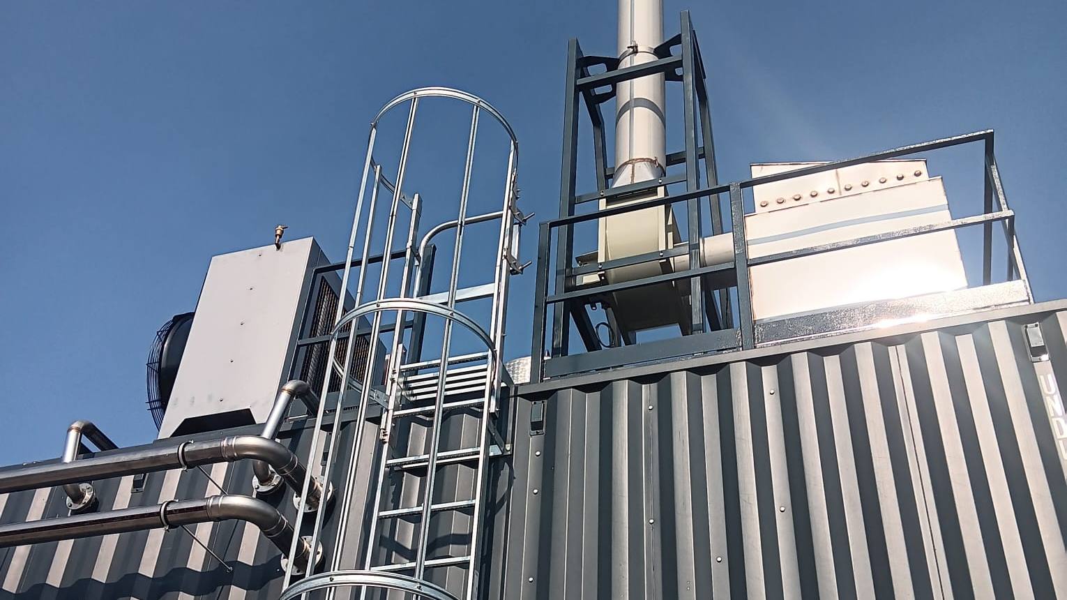 Biomasseverbrennungsanlage in Containerbauweise mit Kamin vor blauem Himmel
